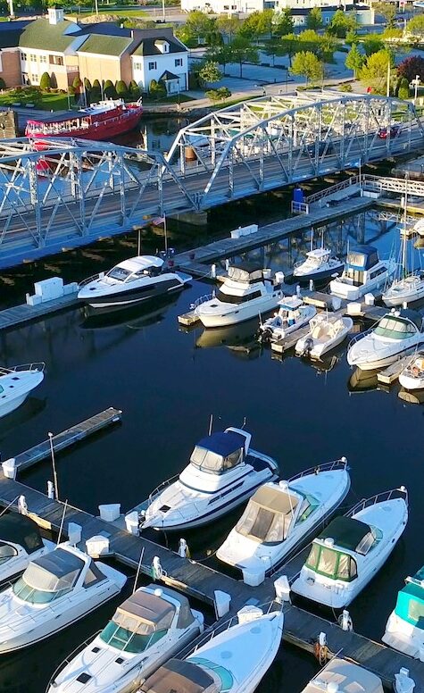 A harbor in the foreground with a bridge over it leading to a quaint lakeside town.